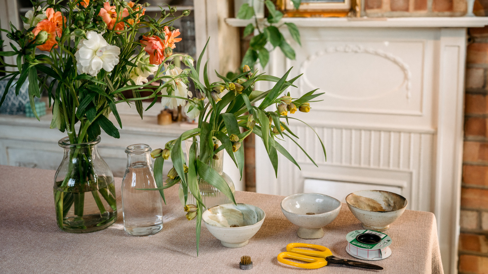 Table with flowers, three ceramic bowls, scissors, florist tack and a pin frog in florist workshop