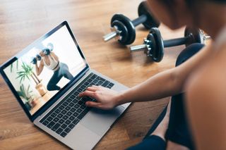 A woman following a dumbbell workout on her laptop with a pair of dumbbells.