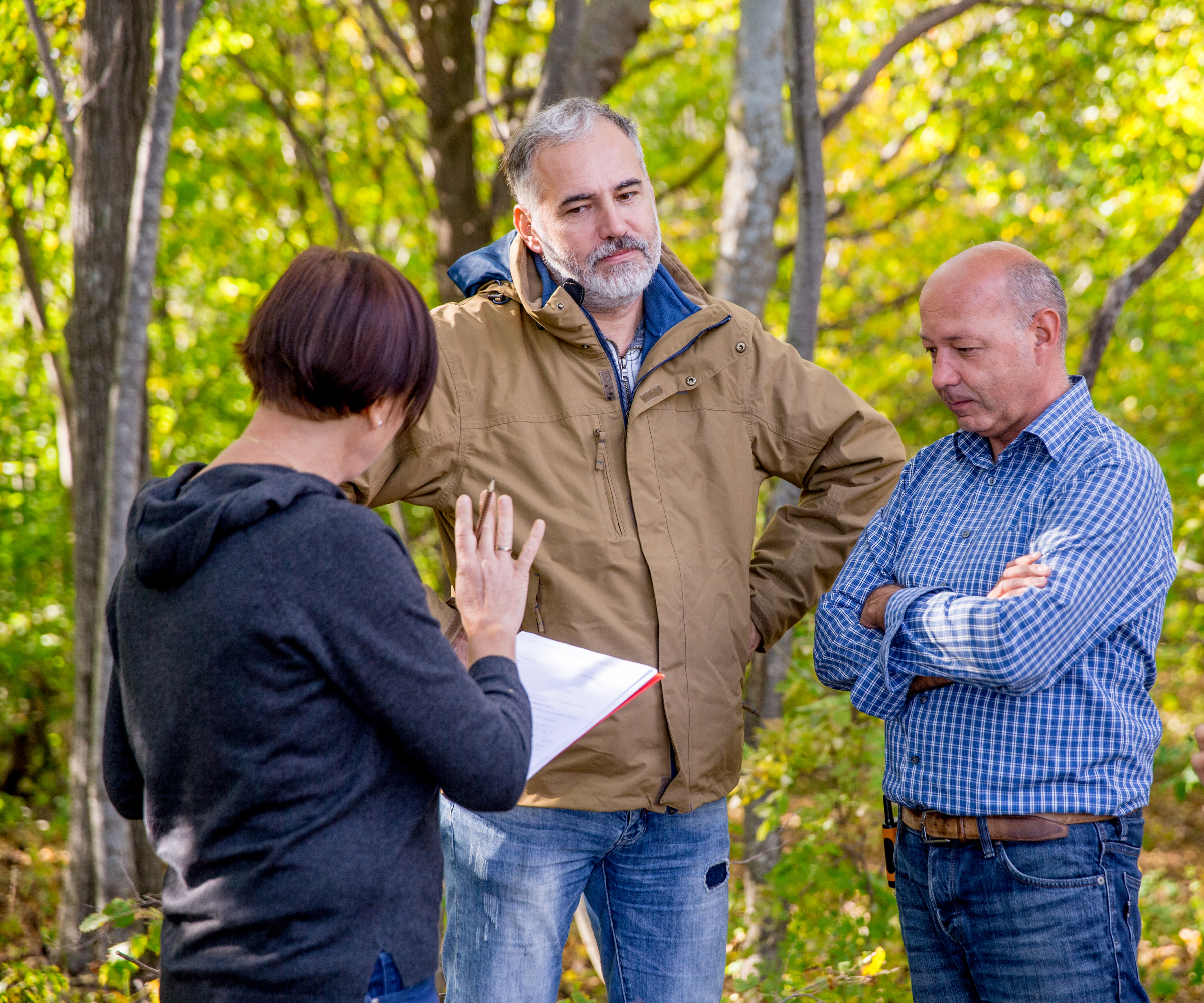 two males, one female stood in garden with trees talking