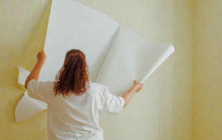 Back of a woman removing wallpaper from a wall