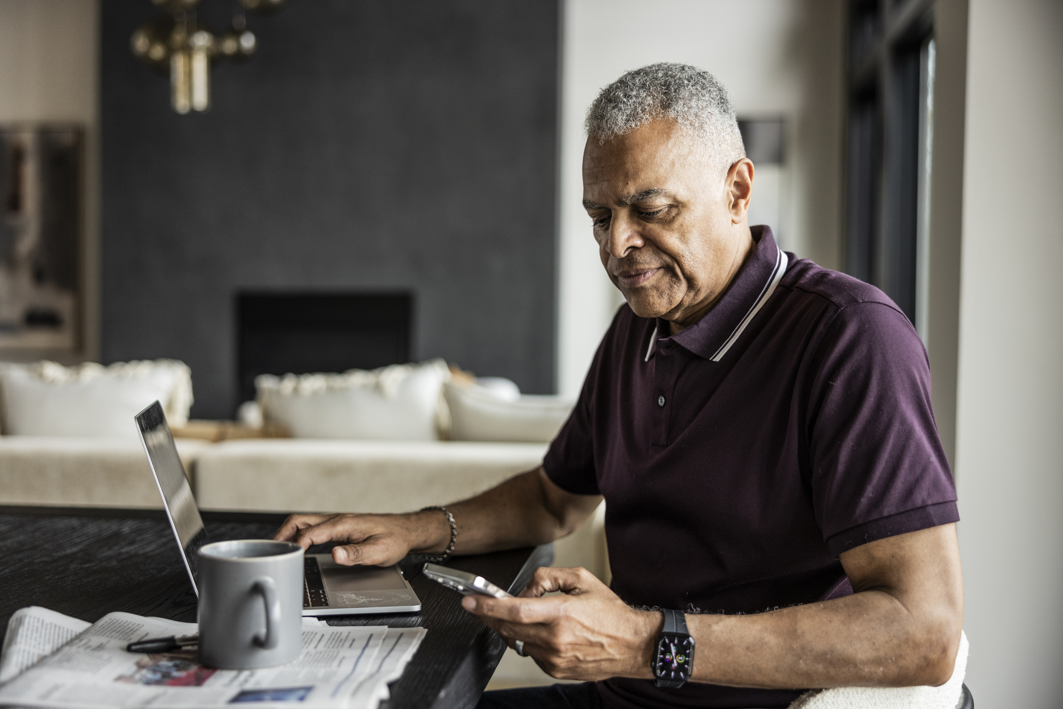 Senior man using smartphone and looking out window at home
