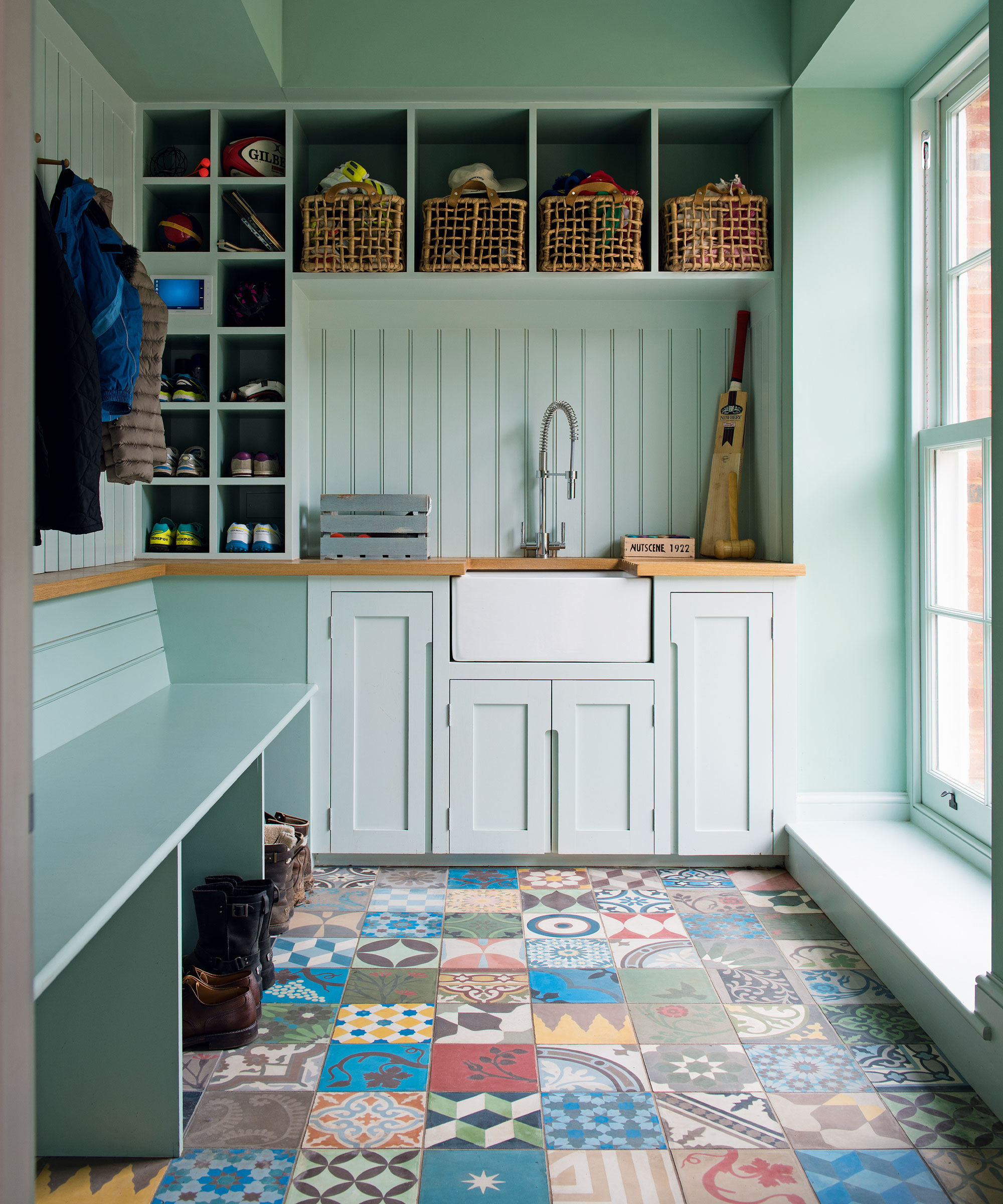 Boot room with eye-catching tiles in patchwork design. Blue painted walls, cabinets and bench, wicker storage baskets, sink