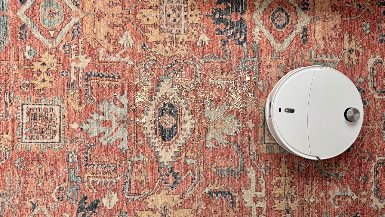 Roborock Qrevo Curv 2 Pro on a patterned carpet rug, with oats and crumbs sprinkled in front of it