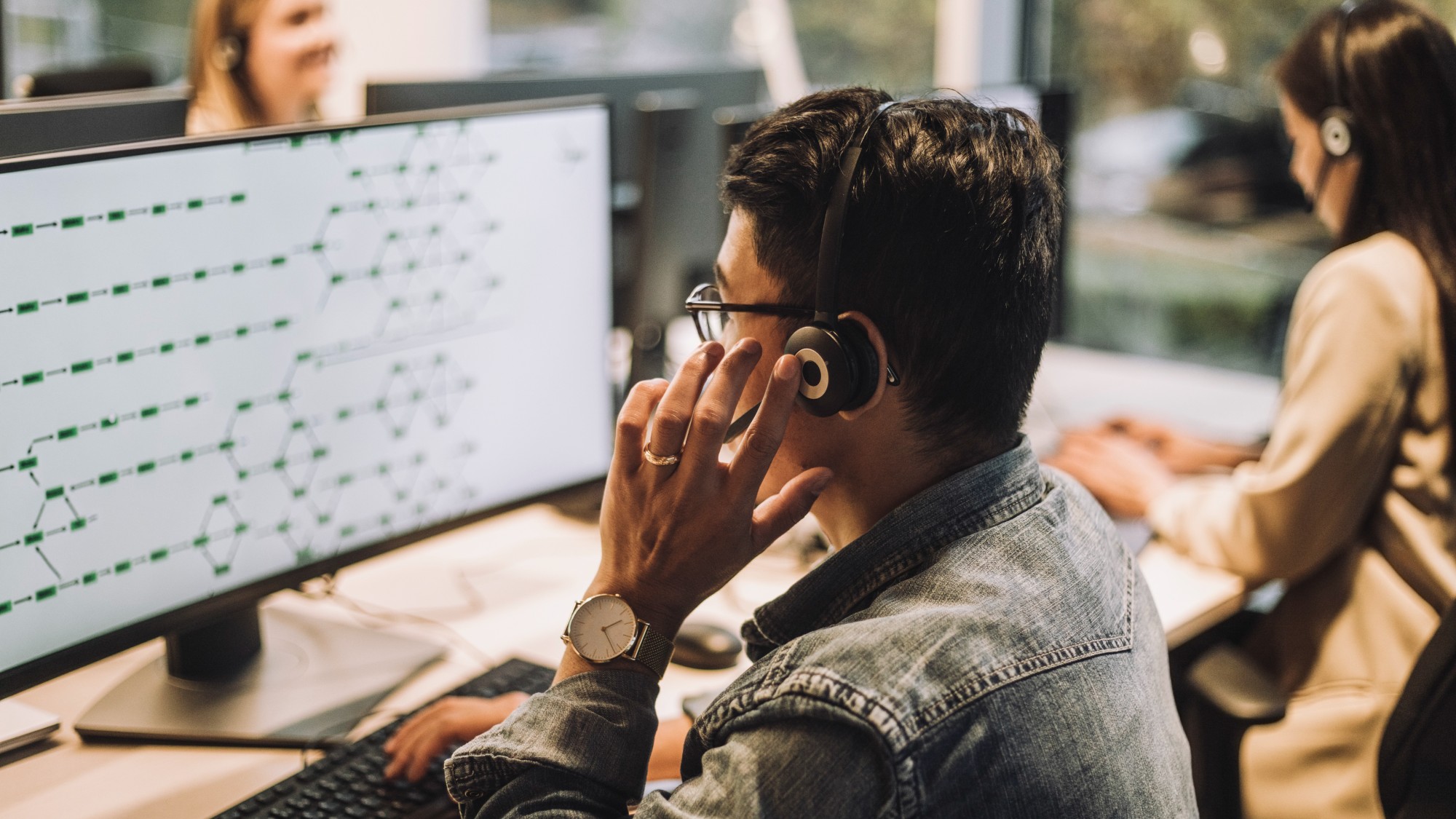 Young male customer service employee using computer talking through headset at call center