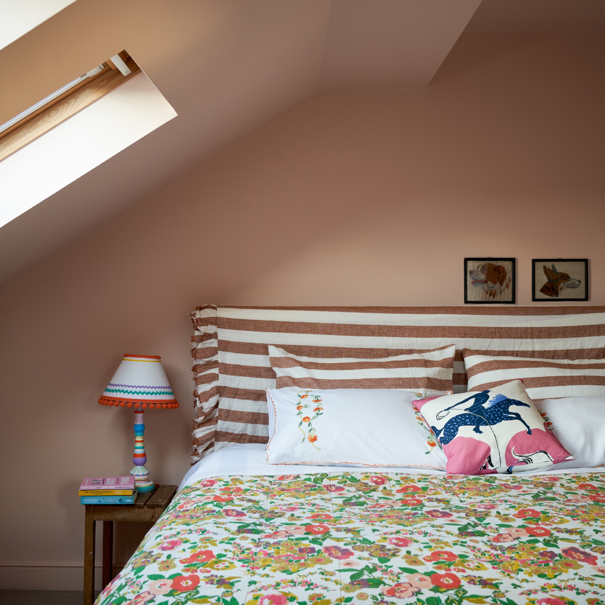 A bedroom with a striped-headboard bed and floral bedspread, painted in Farrow &amp;amp; Ball's Pink Ground shade