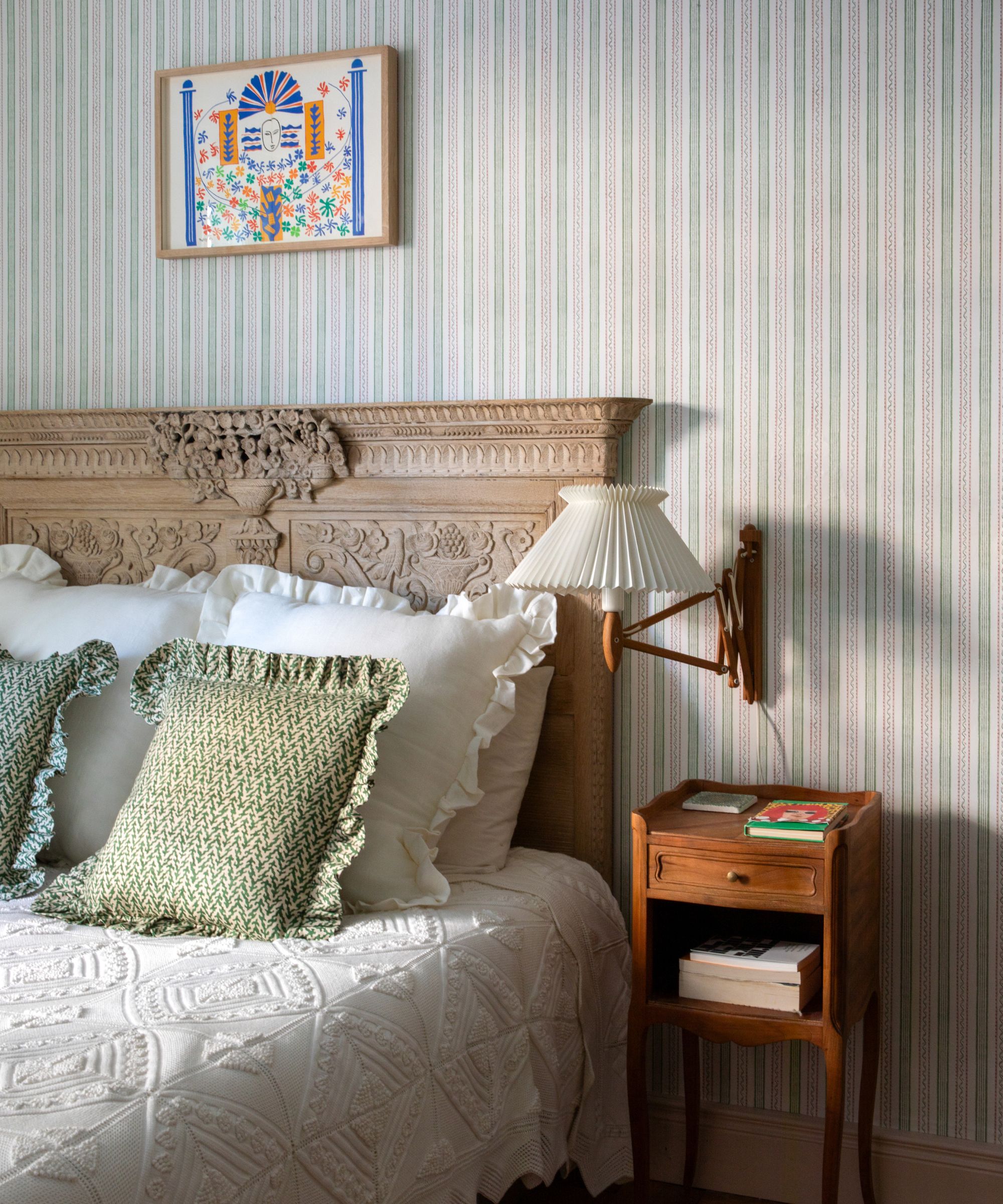 A traditional bedroom with blue stripped wallpaper and a carved wooden headboard bed.