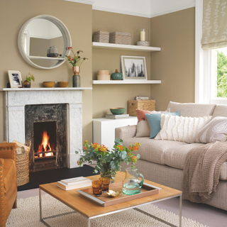 Living room with a lit fire in a traditional fireplace, shelves and a cupboard, large sofa and cosy painted walls.