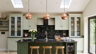green kitchen island with copper pendant lights over