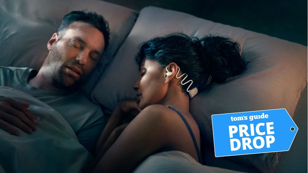 A man and woman sleeping in bed. The woman has her dark hair tied in a bun showing she is wearing the Philips sleep headphones