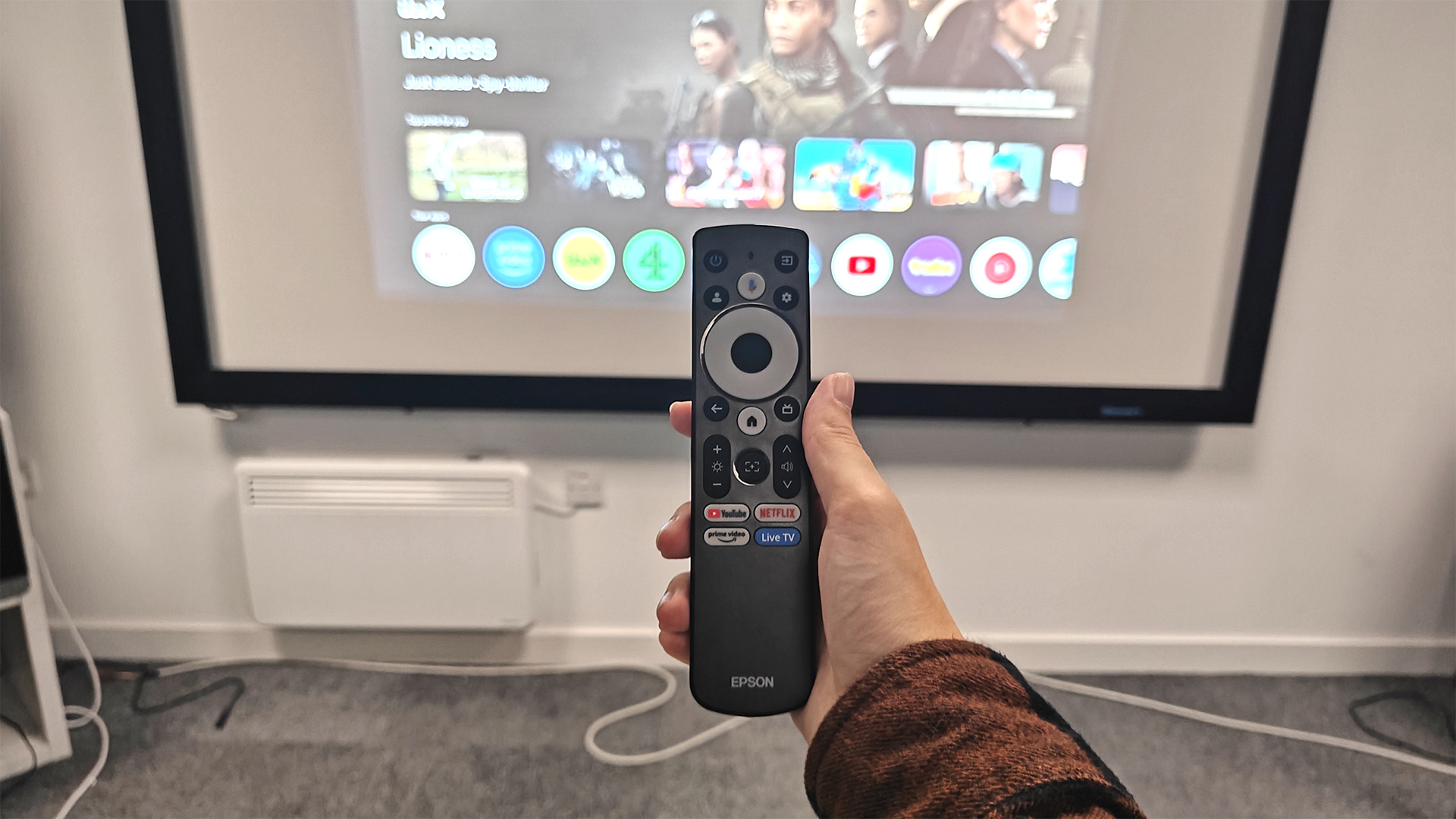 Epson EF-72 home cinema projector remote control held in hand in front of screen