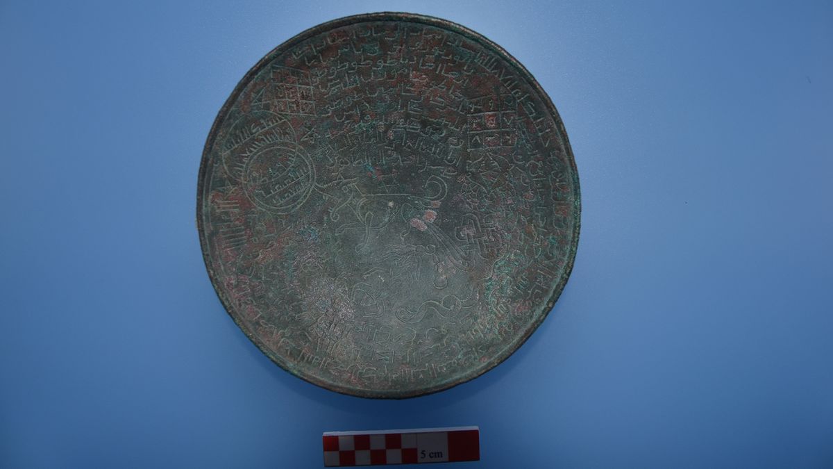 A photo of an inscribed metal bowl against a blue background.