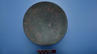 A photo of an inscribed metal bowl against a blue background.