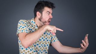 A man shouting and pointing angrily at the smartphone in his hand.