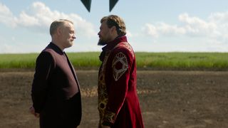 two men stand together in a dirt circle beside a grassy field