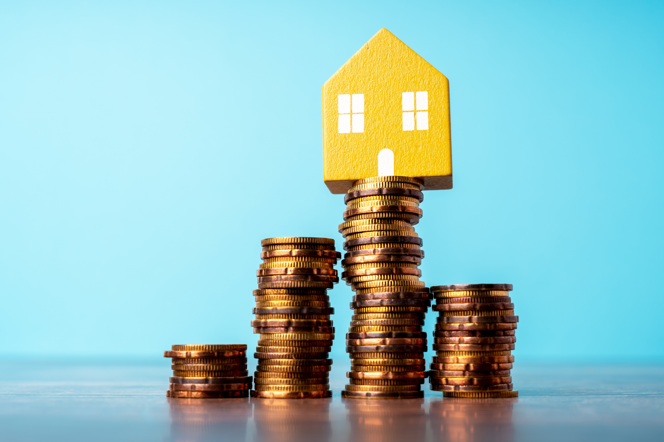 miniature yellow house on a high stack of coins surrounded by other stacks of coins