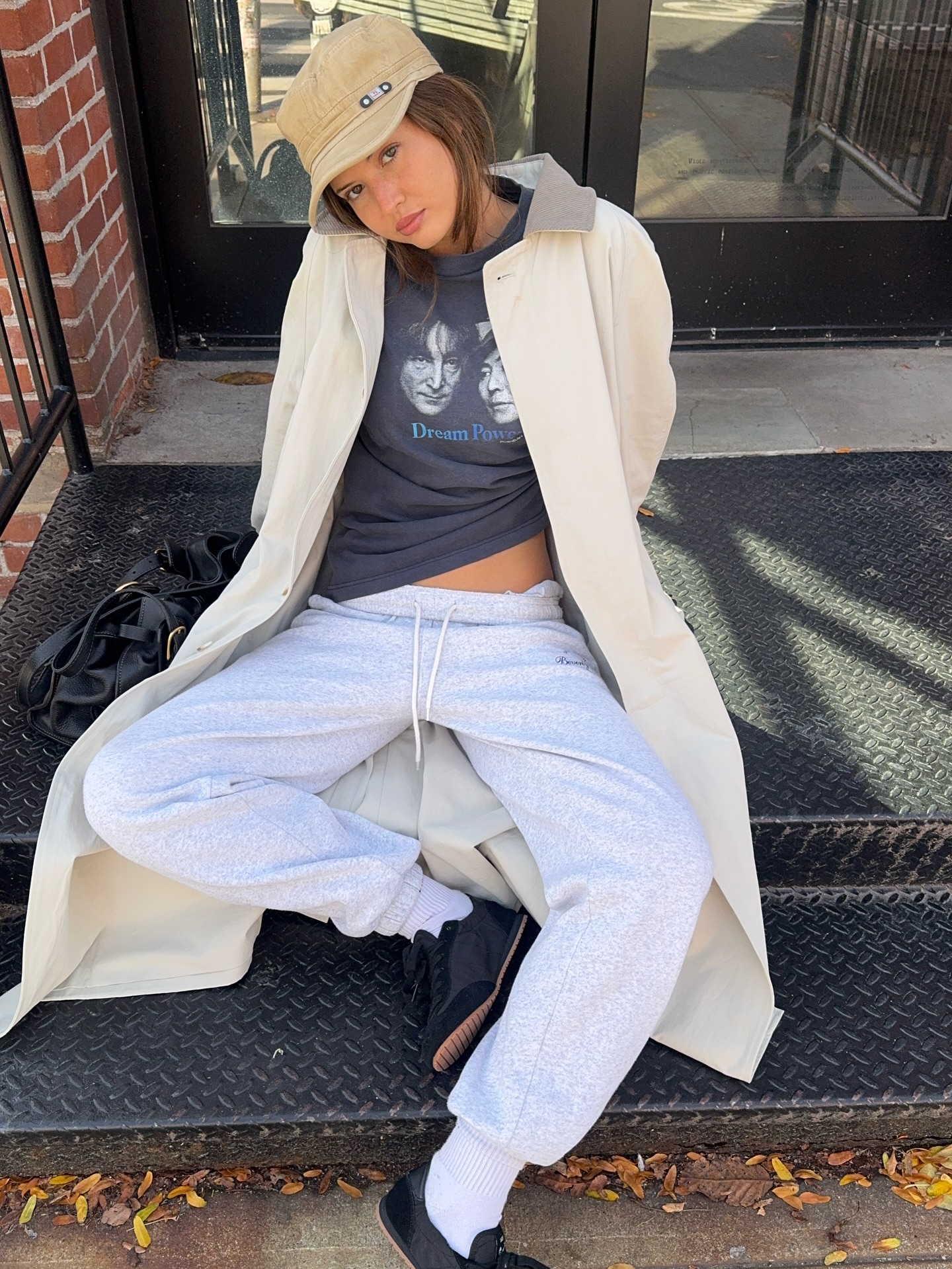 Influencer Ruby Lyn wearing trench coat, graphic tee, hat, and gray sweatpants with black ballet sneakers.