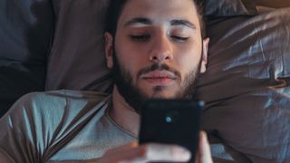 bedtime revenge procrastination: a man scrolls on his phone in bed when he should be sleeping