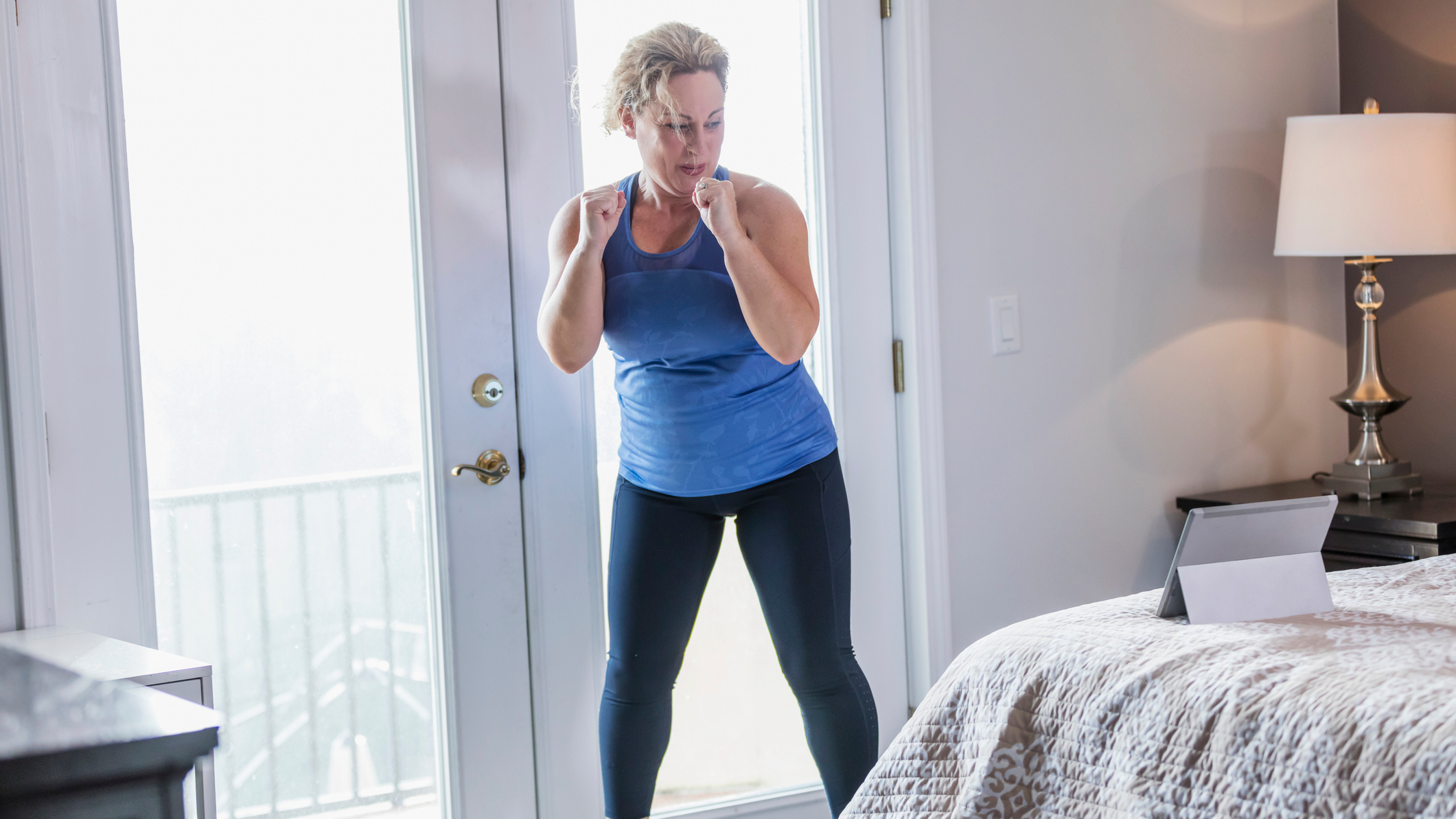 Woman exercising at home looking at a tablet resting on a bed
