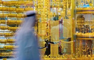 A man in a white robe walks in front of gold jewelry at Dubai's Gold Souk