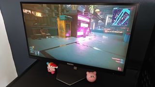 AOC AGON Pro AG246FK gaming monitor with Cyberpunk 2077 gameplay on screen featuring glowing neon lights