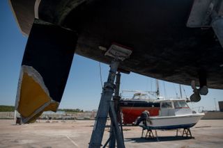 a boat with a broken rudder propped up on a dock with two smaller boats in the background.