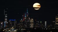 A yellow full moon streaked with clouds shines in a black night sky above the New York City skyline.