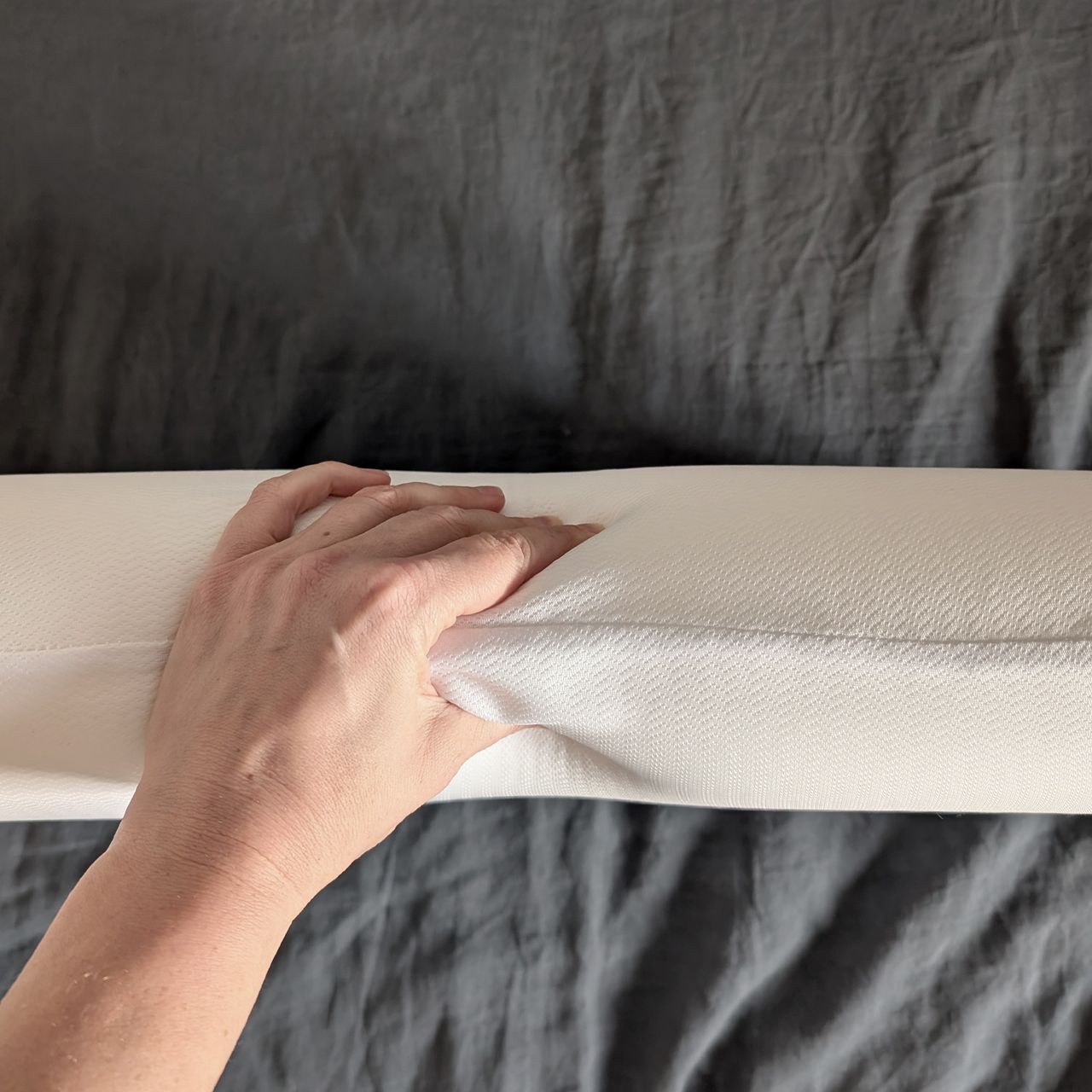 The Levitex Sleep Posture pillow on it's side being squeezed by a hand.