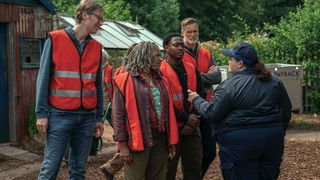 Greg (Stephen Merchant), Myrna (Clare Perkins), Ben (Gamba Cole) and John (Darren Boyd) in hi-vis jackets on a farm talk to Diane (Jessica Gunning) in a supervisor's uniform in The Outlaws.
