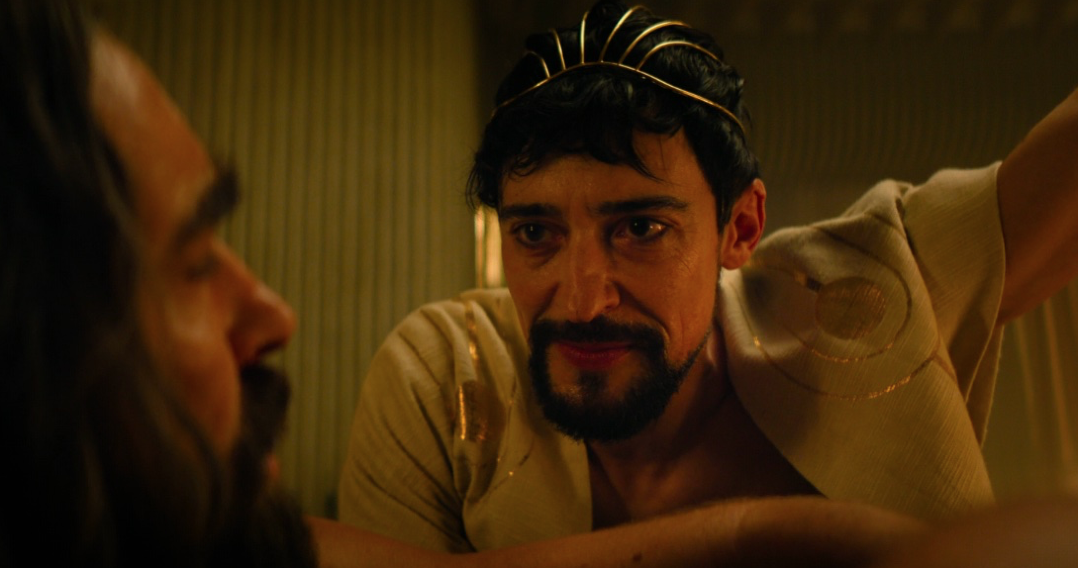 a bearded man in a ceremonial robe interrogates another bearded man