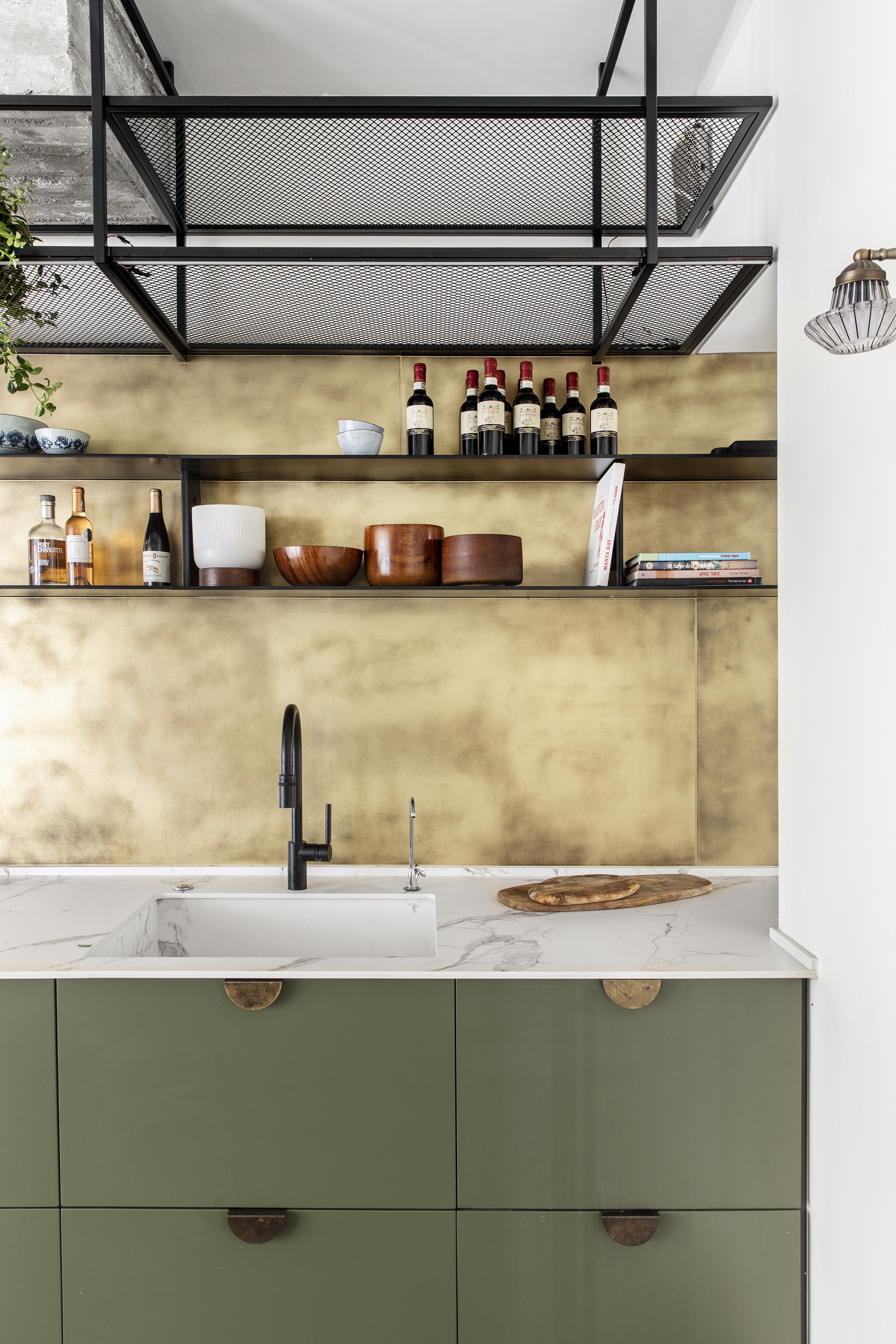 A small kitchen with green cabinets, hanging storage and brass backsplash