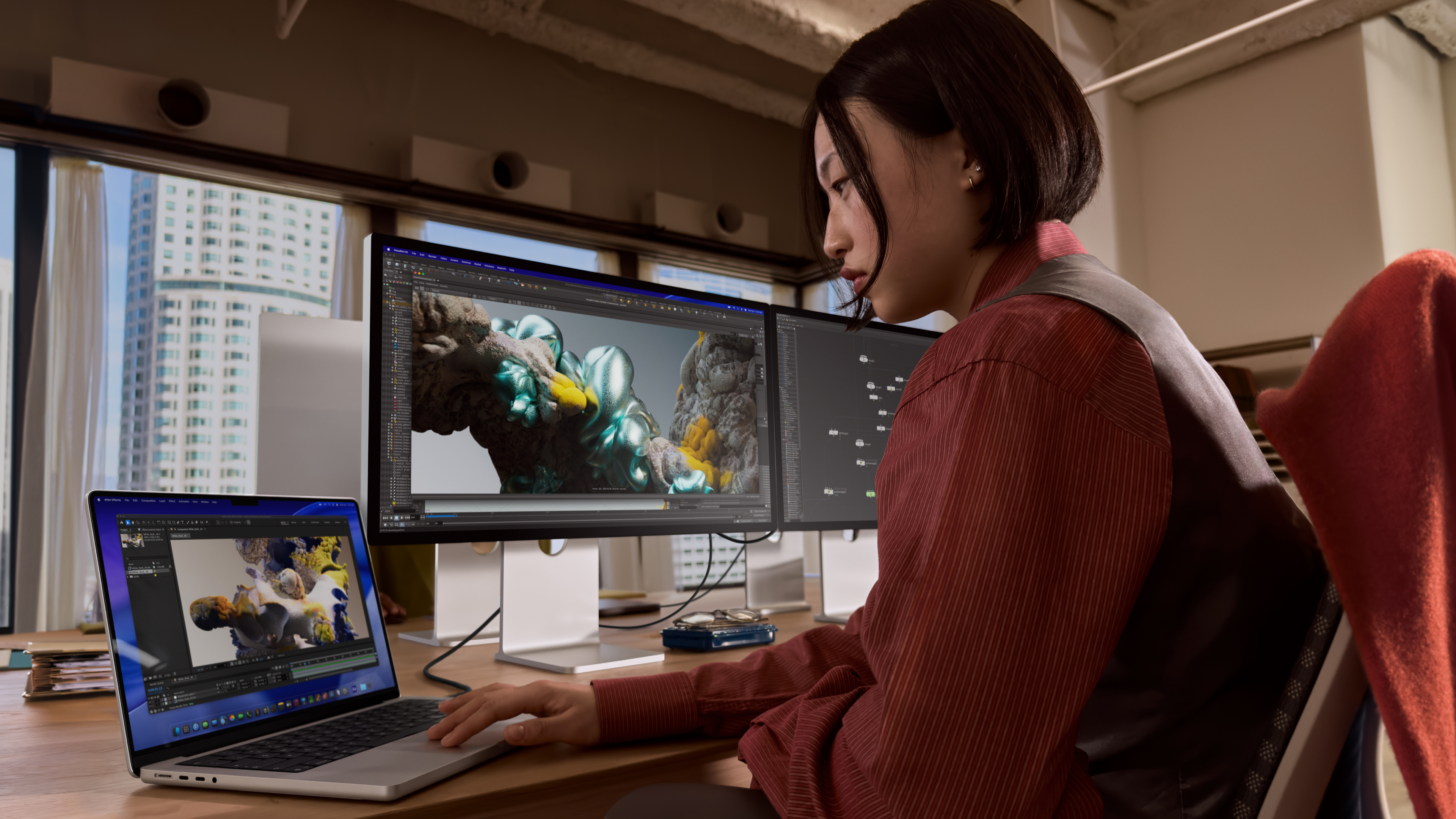 A woman working on a laptop in front of two Apple Studio Display XDR screens in an office