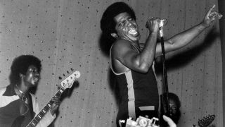 American soul singer and songwriter James Brown (1933-2006) performs live on stage with the J.B.'s, including bass guitarist Bootsy Collins on left and guitarist Catfish Collins (1943-2010) behind on right, in East Ham, London in March 1971.