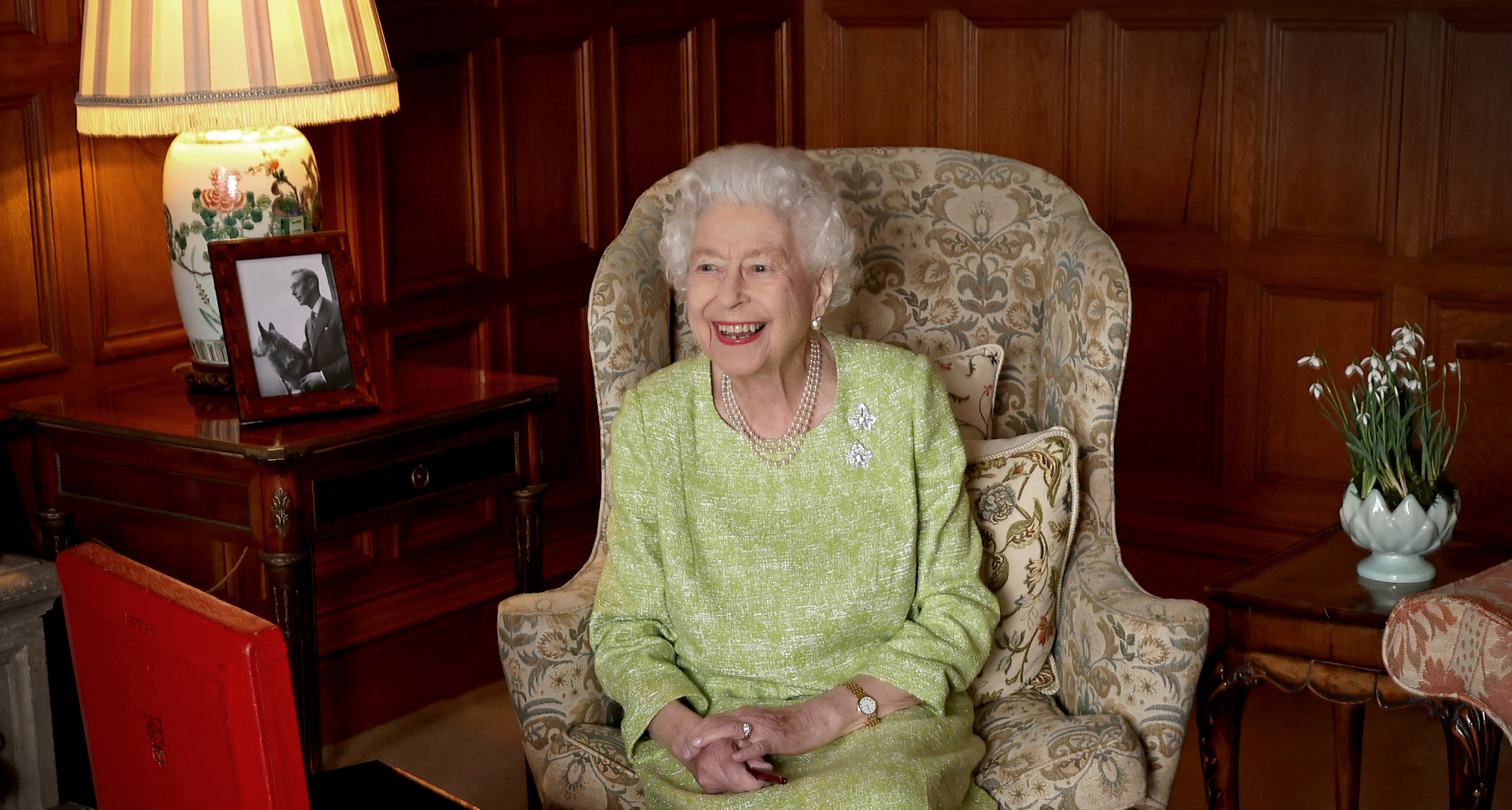 Queen Elizabeth sitting in a chair in a green dress and laughing
