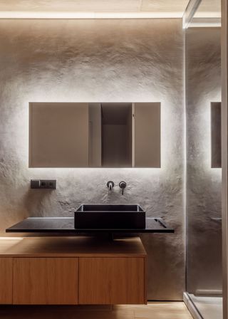 A mirror with lighting behind it. Under the mirror is a sink with cabinets.