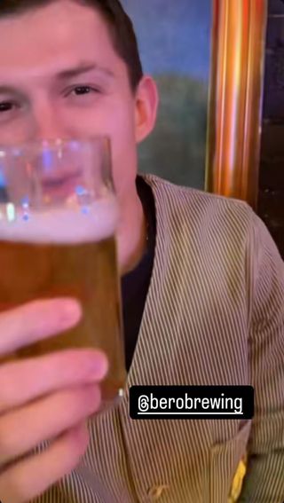 A photo of Tom Holland wearing a striped jacket while sampling his non-alcoholic beer brand.