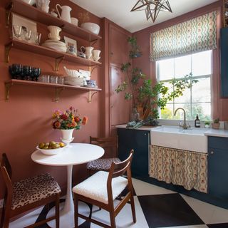 small kitchen with terracotta painted walls, dark blue units, matching sink skirt and blind and small round table