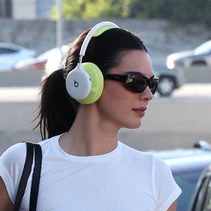 Kendall Jenner has a high ponytail and Beats headphones and wears an all-white outfit while carrying a dog in her handbag