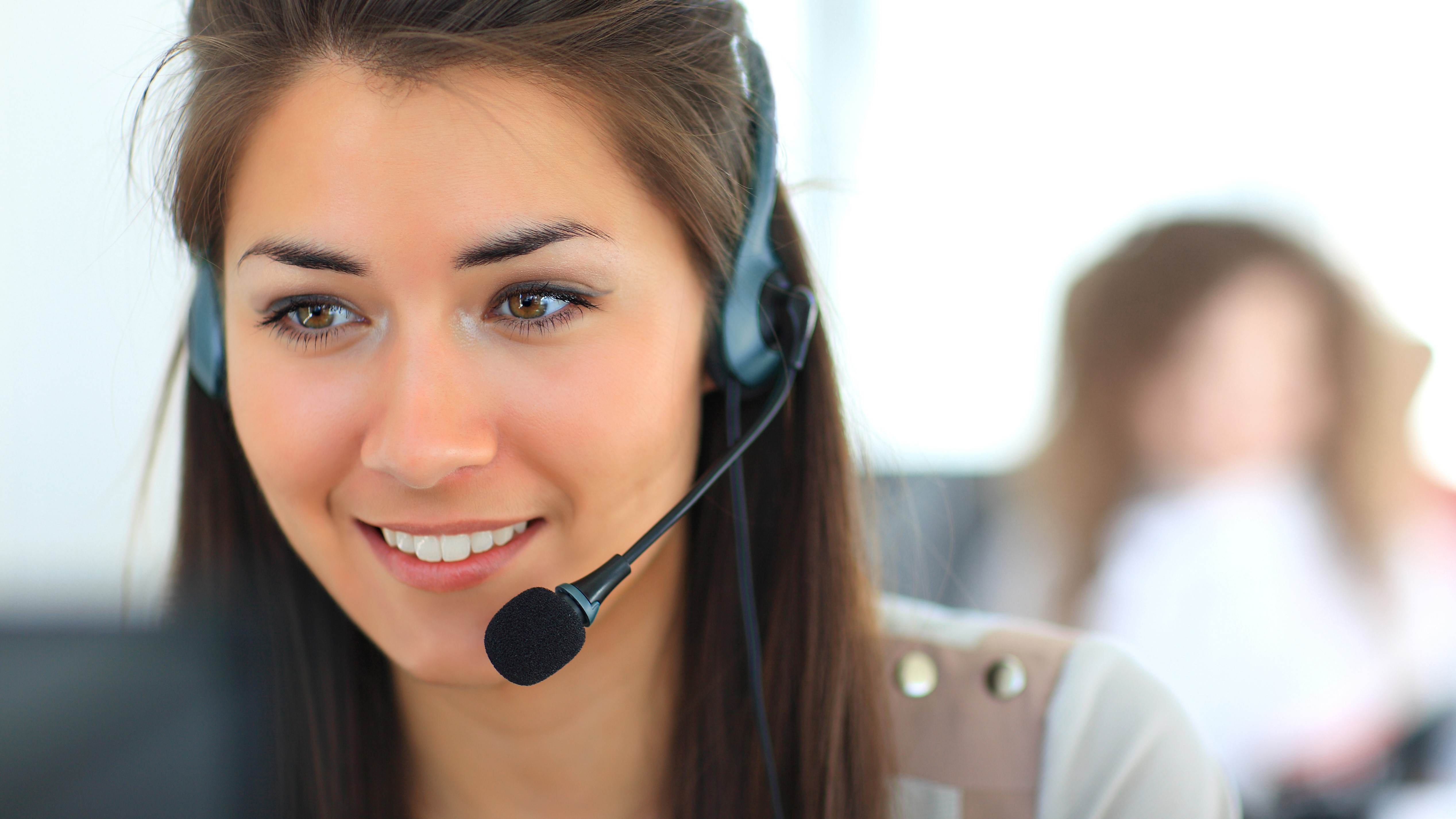 A close up on a woman working at a computer, wearing a headset and smiling