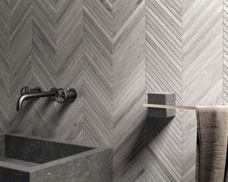 Gray diagonal bathroom tiles by Lapicida behind a gray stone sink.