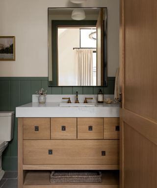 bathroom with green panelled lower walls and white upper half, wooden vanity unit and rectangular mirror