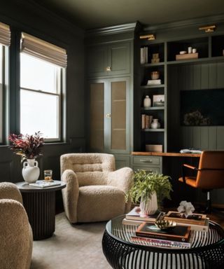 living room with olive green color-drenched walls, built-in cabinets, with desk area, pair of cream boucle armchairs and cozy decor