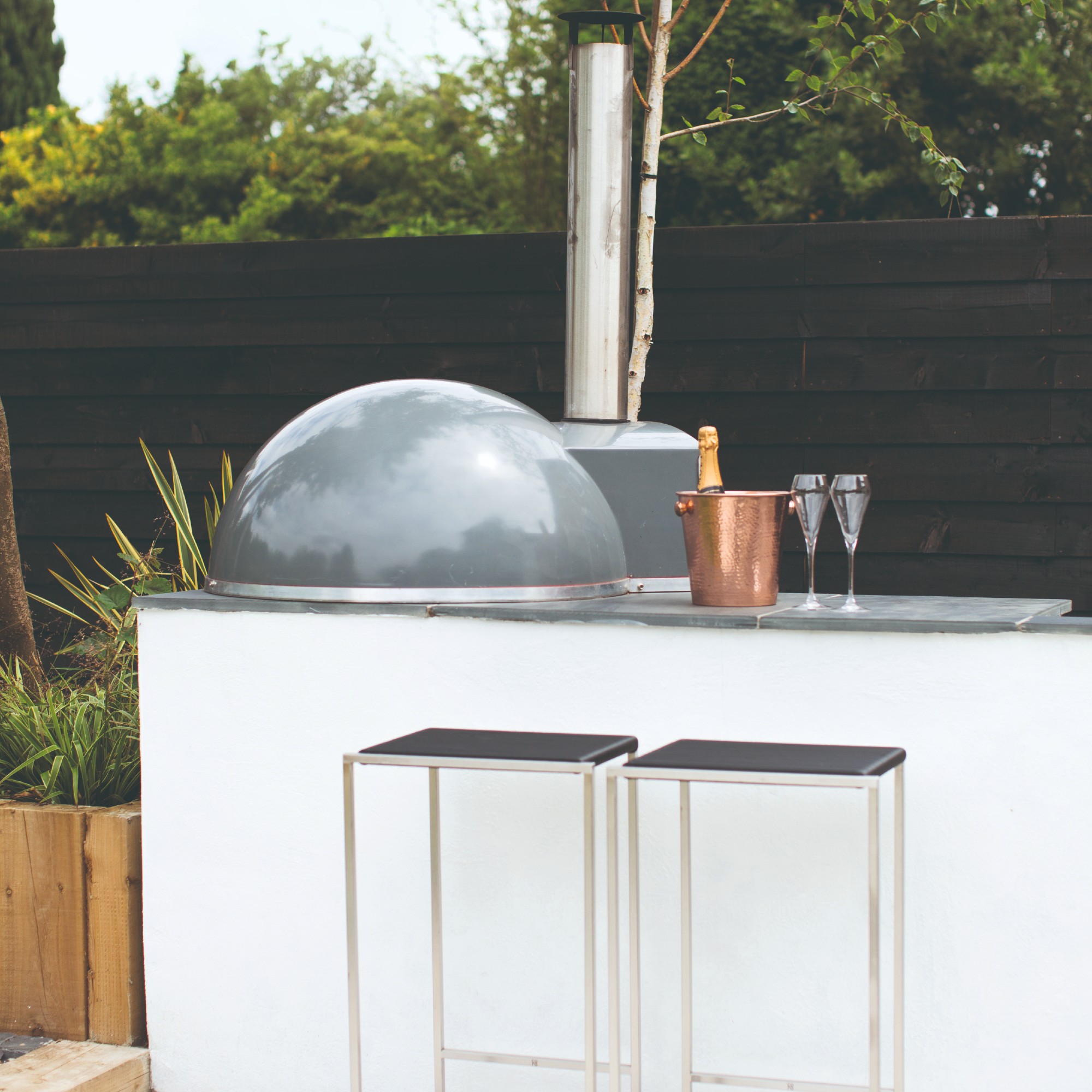 An outdoor kitchen in the garden with seating bar stools