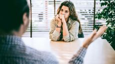 Woman sitting at a desk in the office being scolded by a faceless male boss