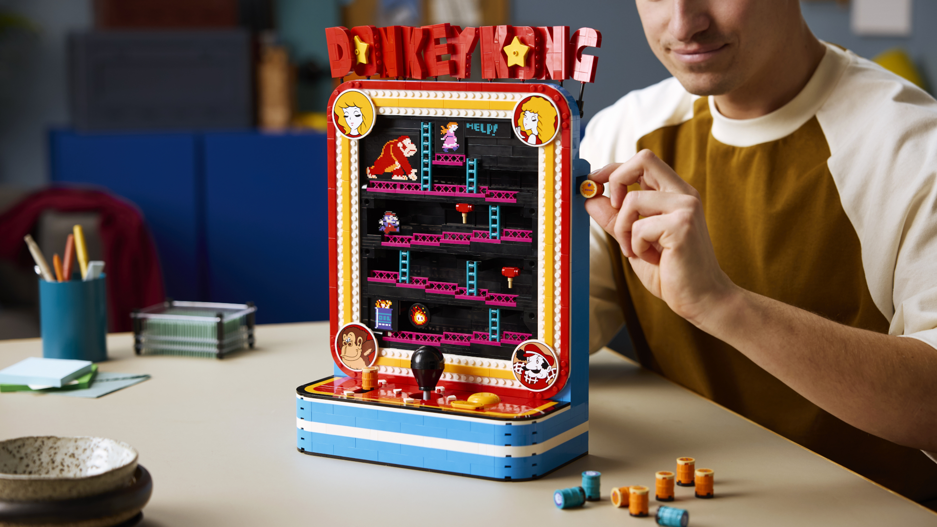 A man puts a barrel into the side of the Lego Donkey Kong Arcade while it stands on a pale table