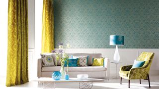 living room with patterned metallic turquoise wallpaper with citrus colored curtains to the floor to show the how to avoid common interior design mistakes with short curtains