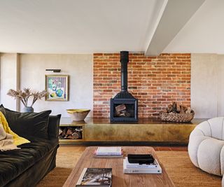 open plan living space with rush rug, velvet sofa, wooden coffee table, inbuilt brass console and fireplace with exposed brick wall behind