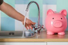 Flowing tap water and a piggy bank standing next to it. Water consumption price concept