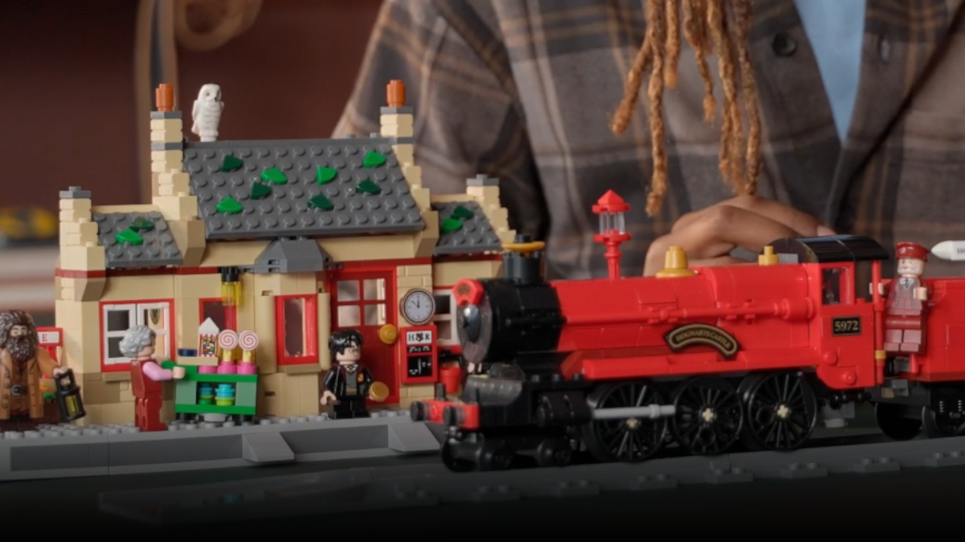 Lego Hogwarts Express set being played with by a child, while the Hogsmeade Station kit sits in the background