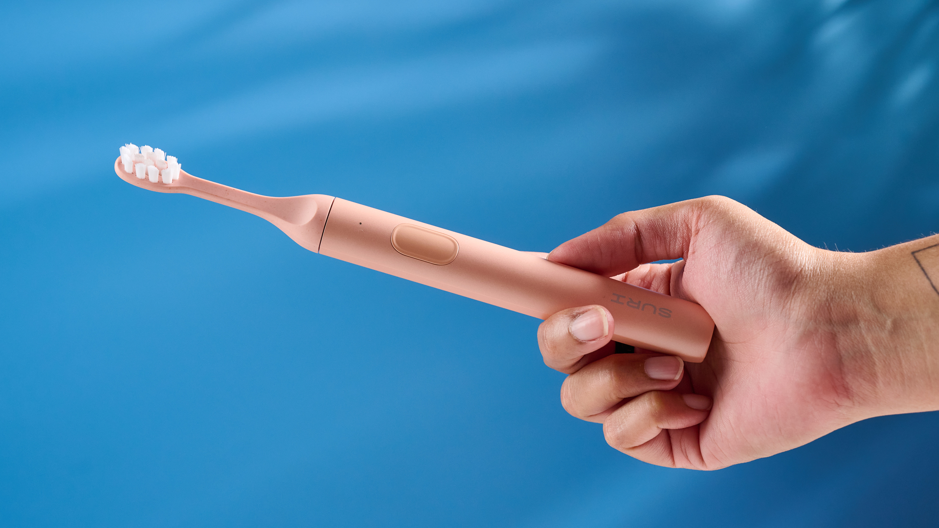 the Suri 2.0 toothbrush in sunset bloom pink colorway with a plant-based head and aluminum body, pictured with its uv cleaning travel case and the suri toothpaste