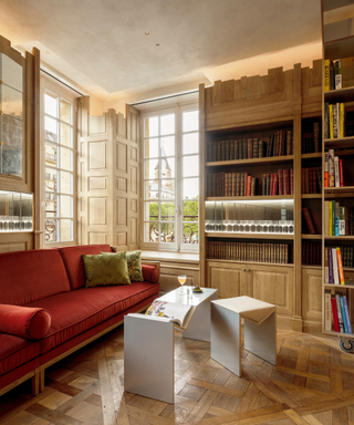 Library room with parquet Versailles floors, red couch and wooden bookshelf